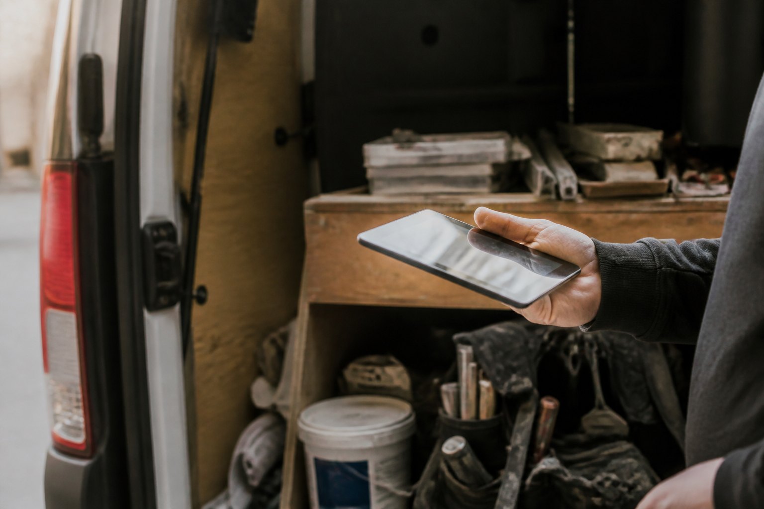 Offener Transporter voller Werkzeug und Material, eine Hand prüft die Lieferung auf dem Tablet